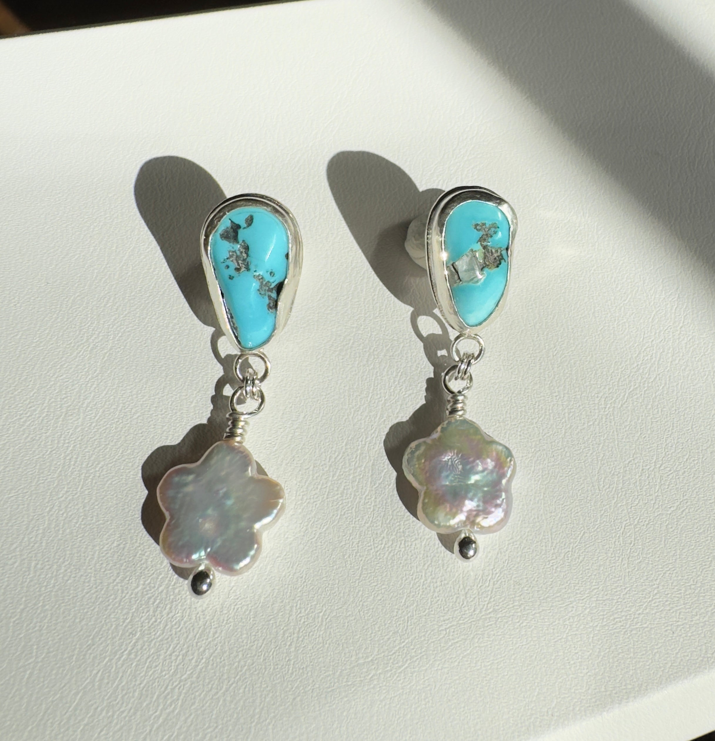 Castle Dome Turquoise set in a fine silver bezel with flower shaped pearls dangling below. The posts and ear backs are sterling silver.