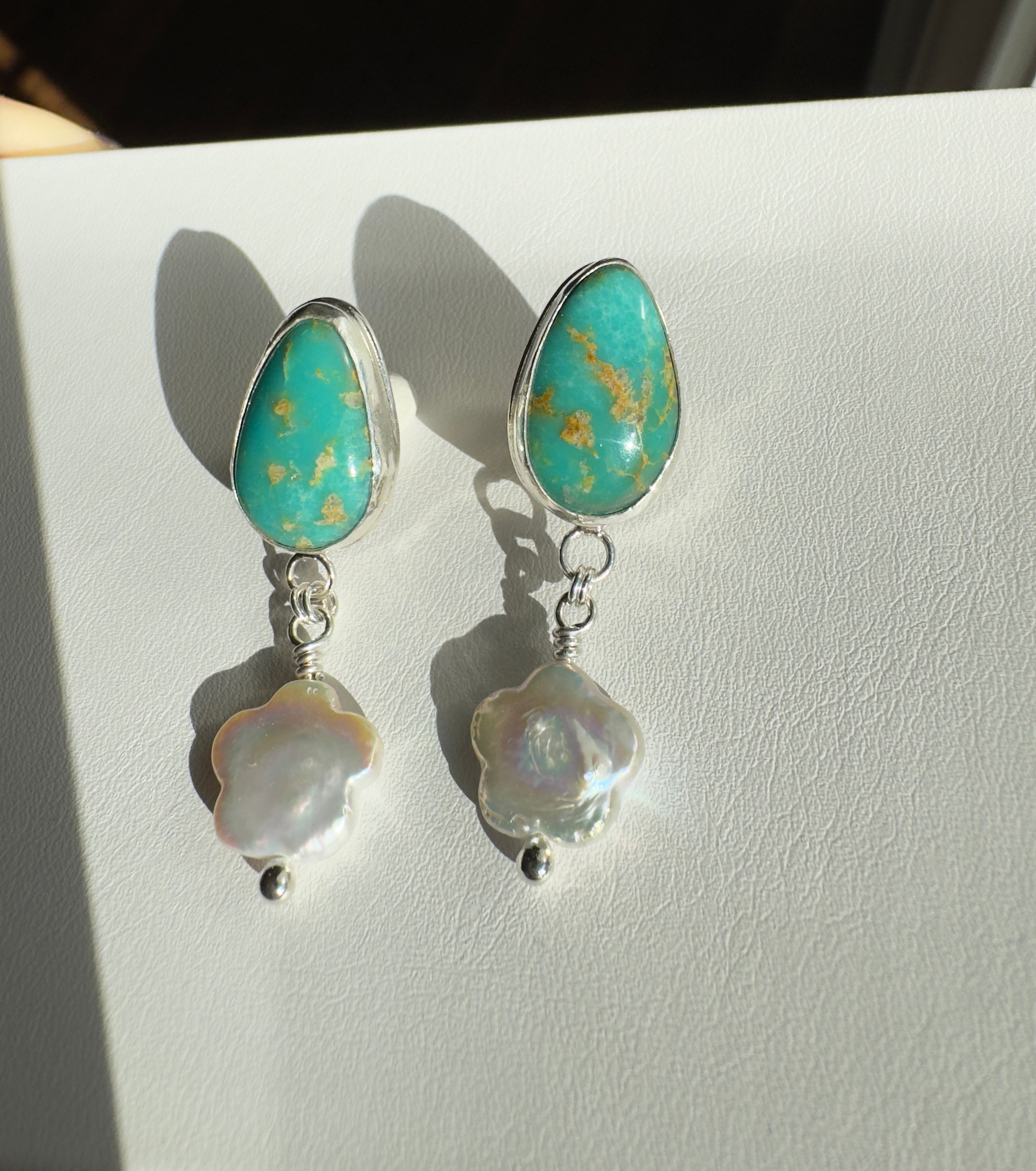 Royston Turquoise set in a fine silver bezel with flower shaped pearls dangling below. The posts and ear backs are sterling silver.