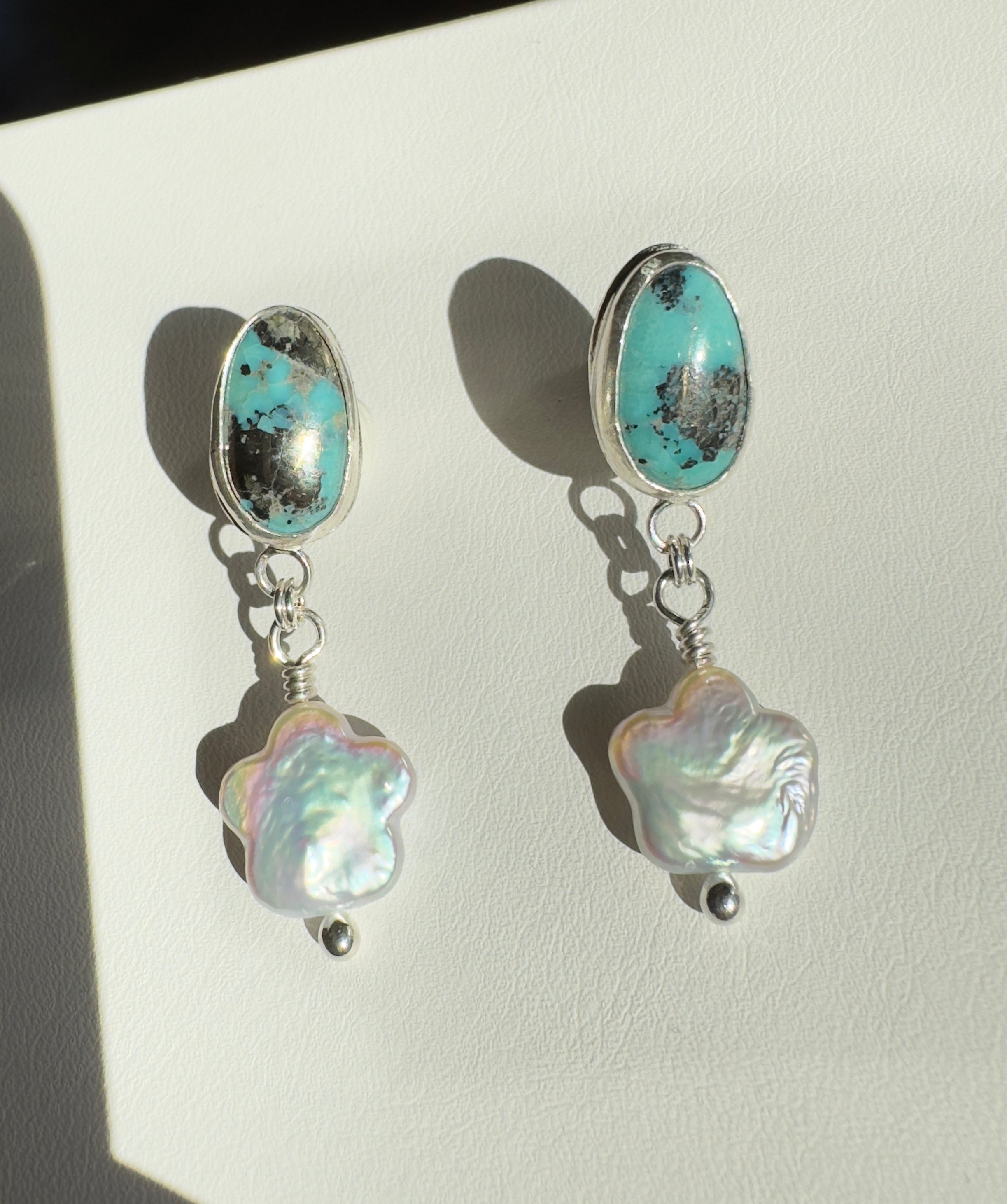 Robin's Egg Blue Kingman Turquoise set in a fine silver bezel with flower shaped pearls dangling below. The posts and ear backs are sterling silver.&nbsp;