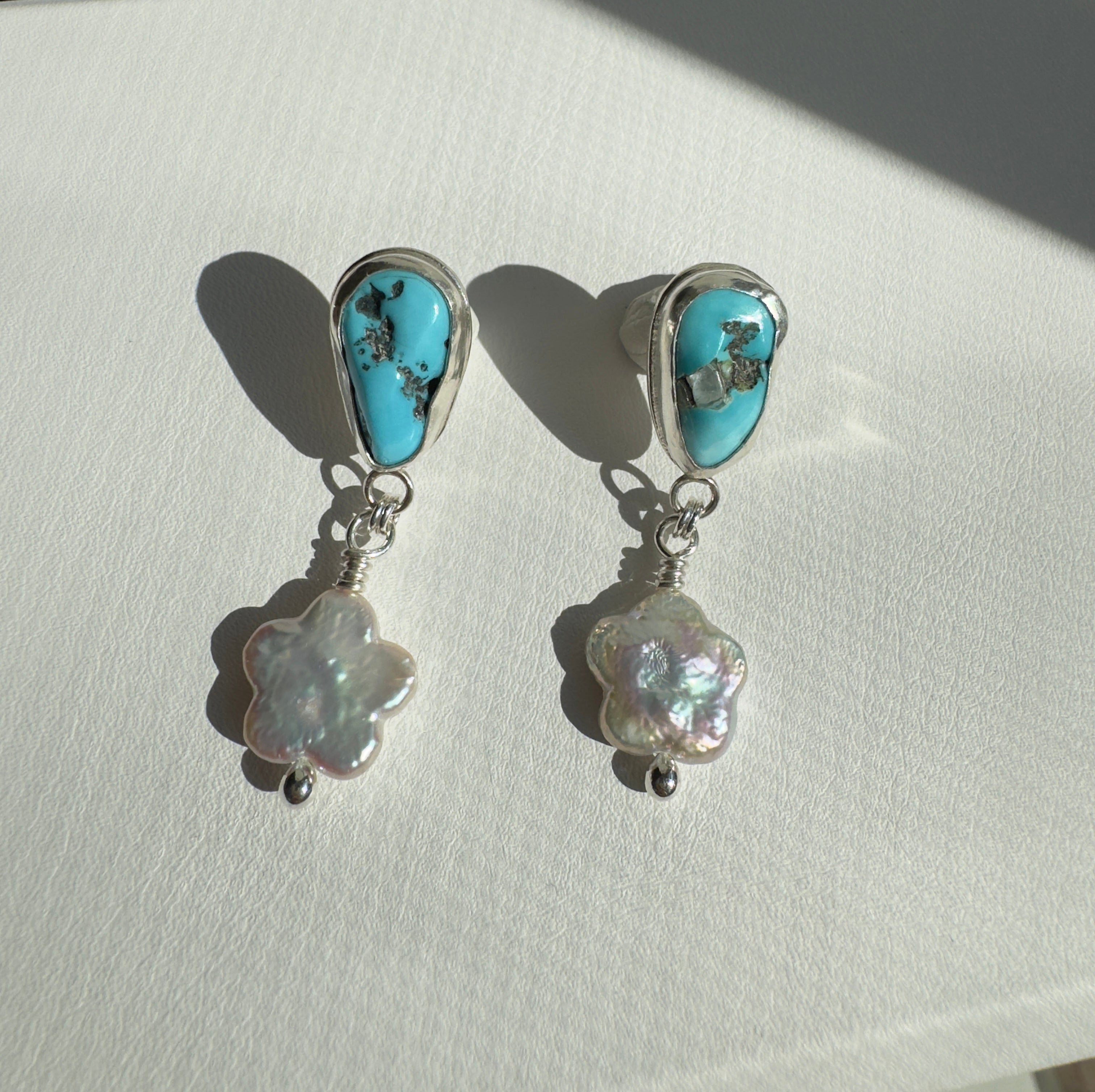 Castle Dome Turquoise set in a fine silver bezel with flower shaped pearls dangling below. The posts and ear backs are sterling silver.