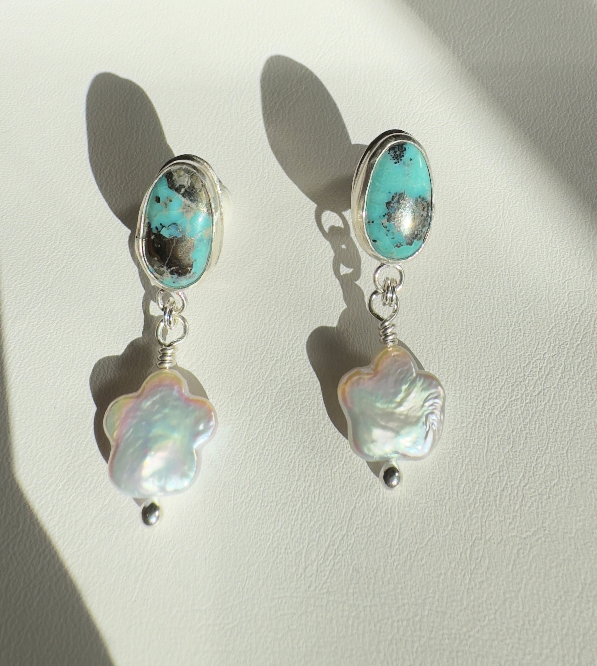 Robin's Egg Blue Kingman Turquoise set in a fine silver bezel with flower shaped pearls dangling below. The posts and ear backs are sterling silver.&nbsp;