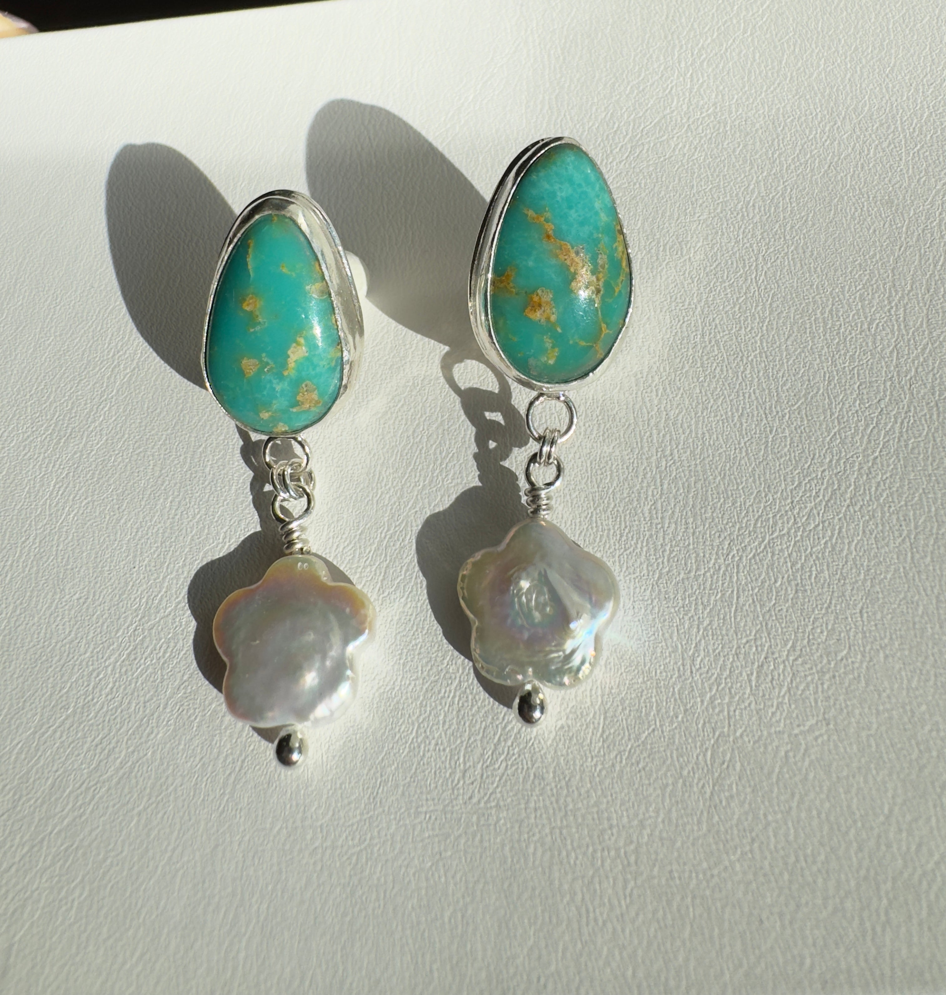 Royston Turquoise set in a fine silver bezel with flower shaped pearls dangling below. The posts and ear backs are sterling silver.