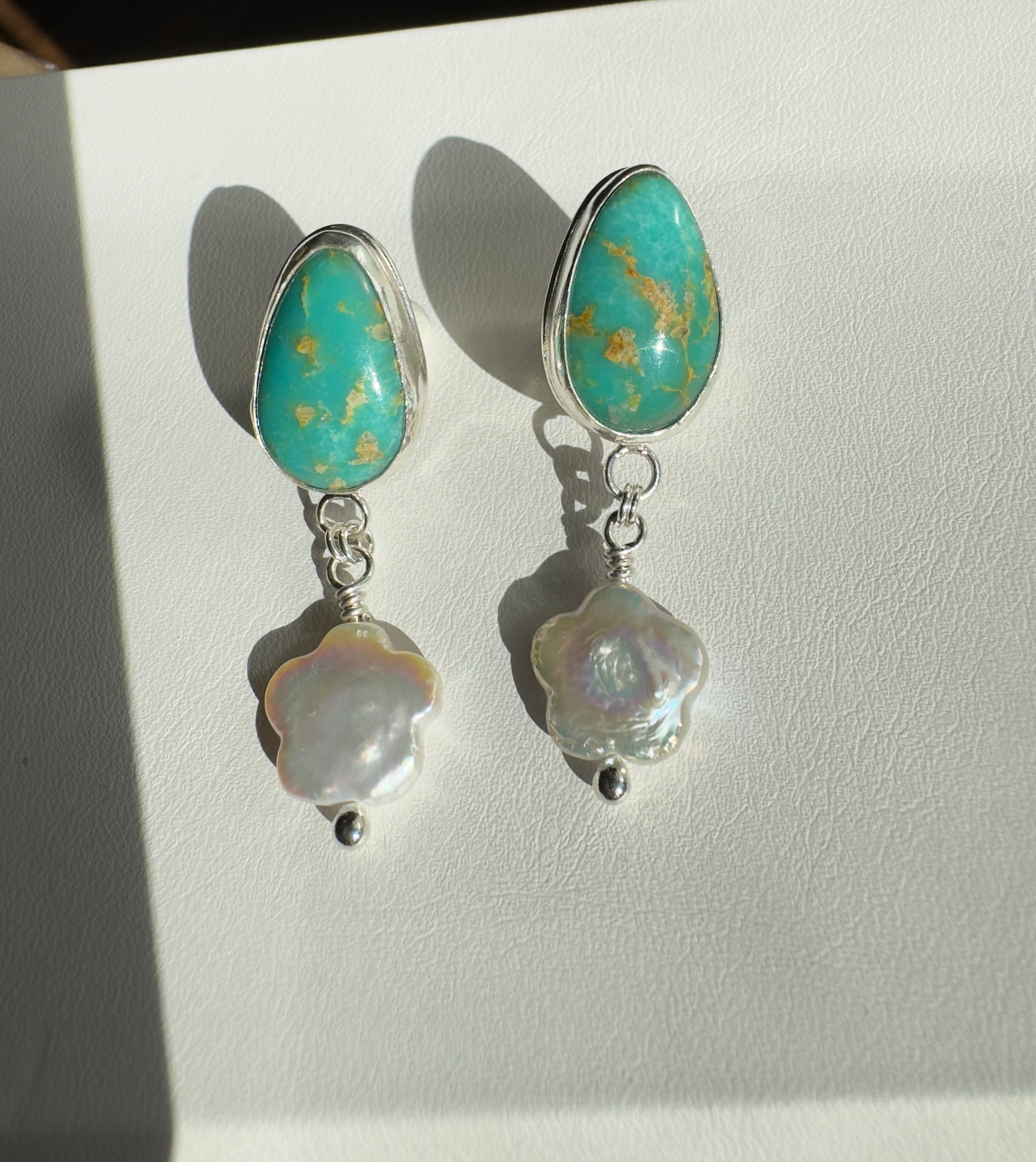 Royston Turquoise set in a fine silver bezel with flower shaped pearls dangling below. The posts and ear backs are sterling silver.