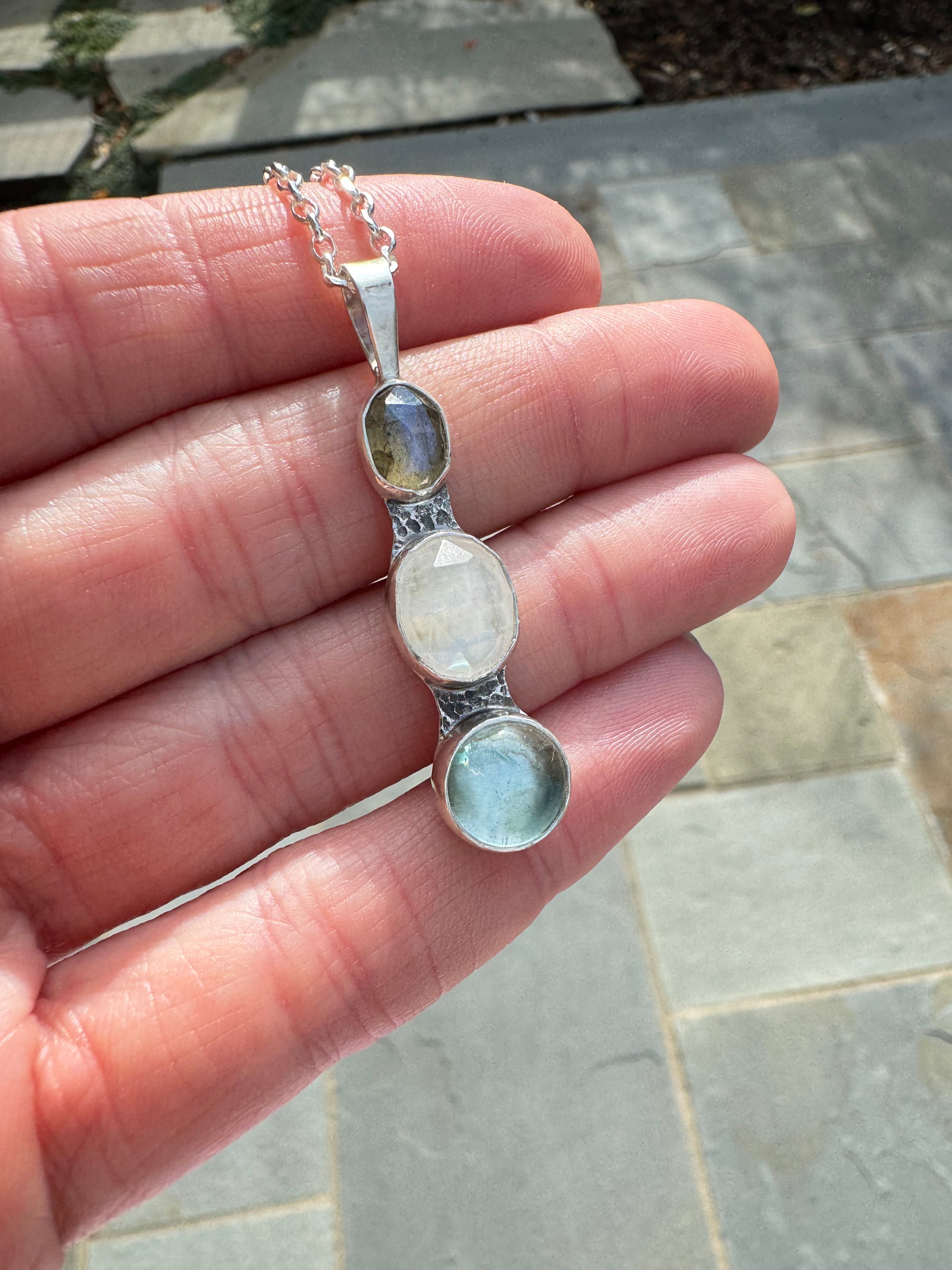 Icy blues of labradorite, moonstone and aquamarine set in fine silver bezels on a sterling silver back. This one of a kind pendant hangs from an 18" 2mm diamond cut Figaro chain.