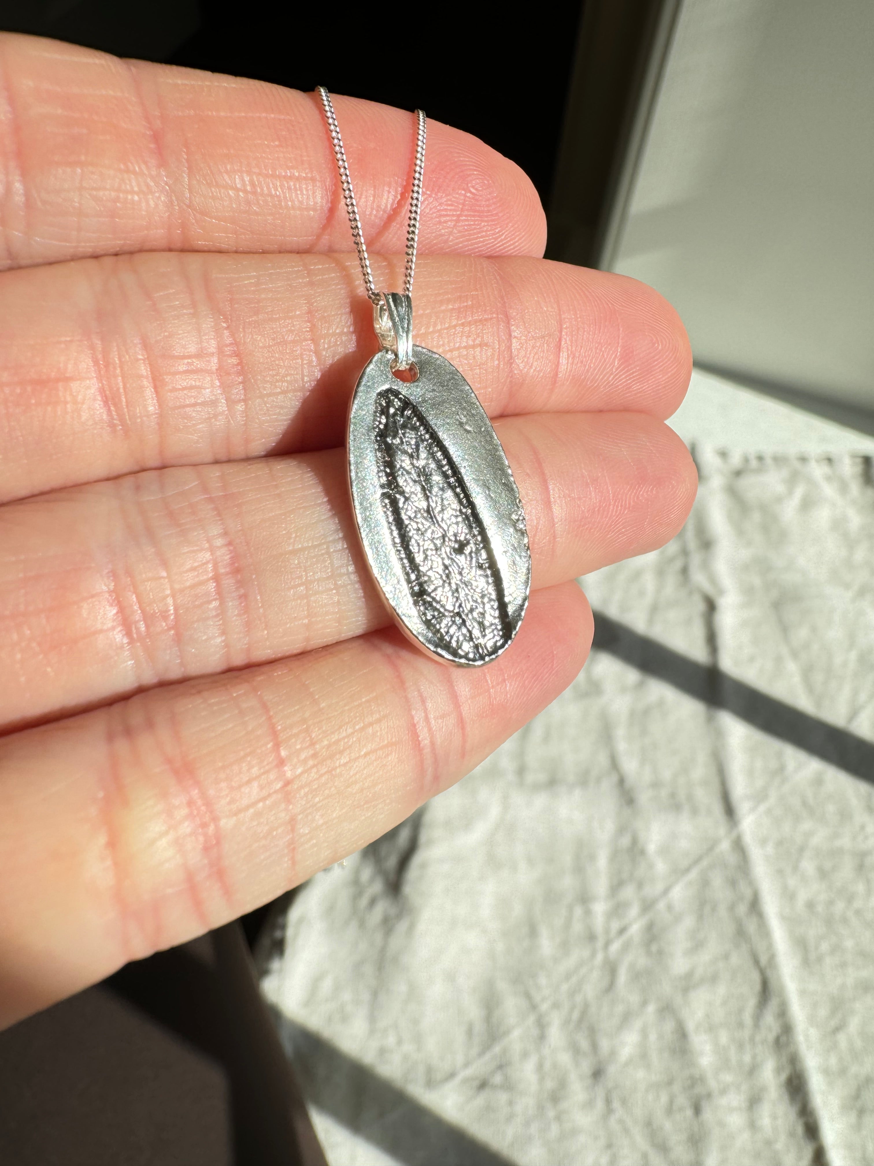 Hand pressed sage on fine silver with a sterling silver bail. Choose between a 16” or 18” sterling silver diamond cut curb chain.